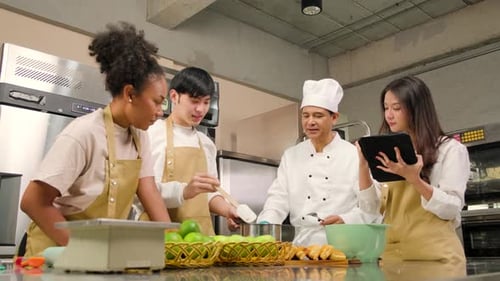 Senior male chef teaches cooking students to prepare ingredients for pastry.