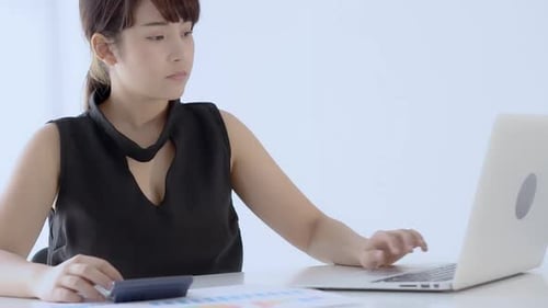 Businesswoman working calculate expenses and typing laptop computer on desk with saving finance.