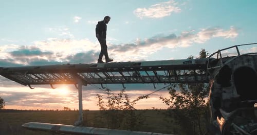 Curious Bearded Tourist Walks Along the Huge Wing of an Abandoned Corn Plane in Deserted Grass Field