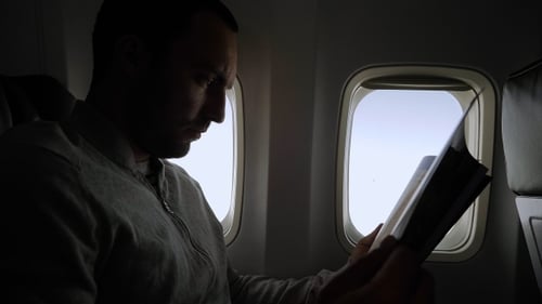 Young man reading magazine in airplane cabin.