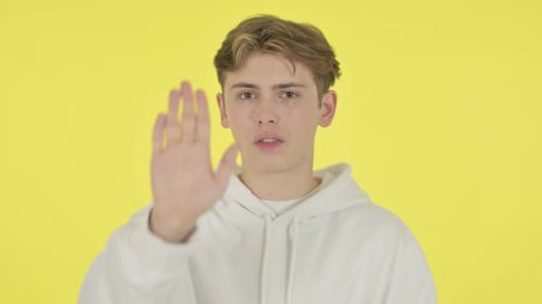 Young Man Showing Stop Sign on Yellow Background