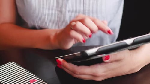 Female Hands Close-up Hold a Tablet. Girl in a Cafe Sitting with a Planet