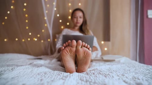 Woman Using Laptop with Feet Up on Bed