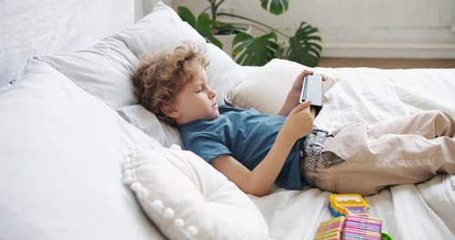 Small Child Watching Cartoons Using Tablet Lying in Bed Alone Relaxing at Home