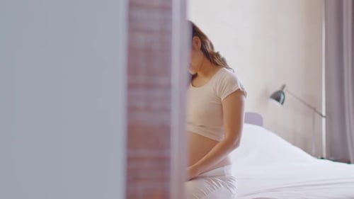 Pregnant Woman Gently Strokes Belly on Bed