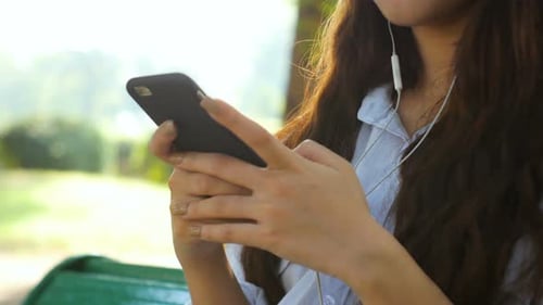 woman is reading pleasant text message on mobile phone while sitting in the park.