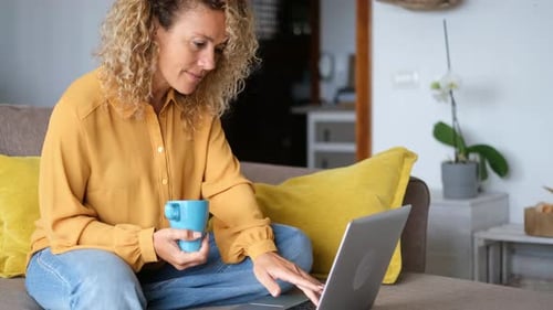 Una mujer joven adulta sonriente se sienta y relájese en el sofá con una computadora portátil moderna