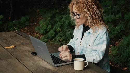 Modern adult female work on laptop computer sitting outdoor in the nature park