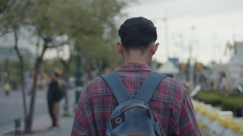 Young Adult Walking with Backpack on Urban Sidewalk