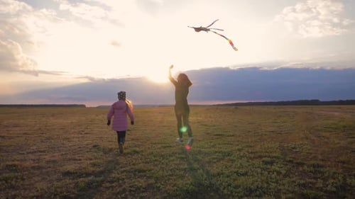 Happy Family Mother and Child Daughter Launch a Kite on Meadow at Sunset. Funny Family Time. Concept