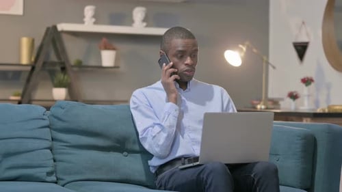 Man Working on Laptop While Talking on Phone