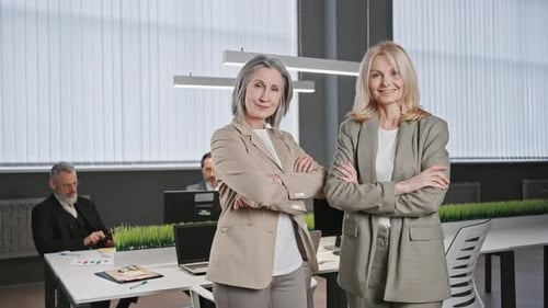 Zoom Out Portrait of Two Confident Mature Ladies Smiling to Camera Posing at Office with Folded
