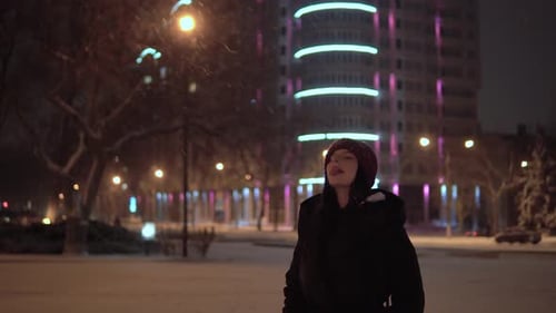 Woman Stands in Snow at Night in City Park
