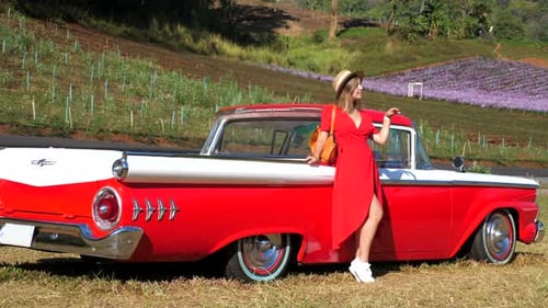 Attractive Young Stylish Woman in Dress Standing Near Red Retro Sports Car on Country Road on Sunny