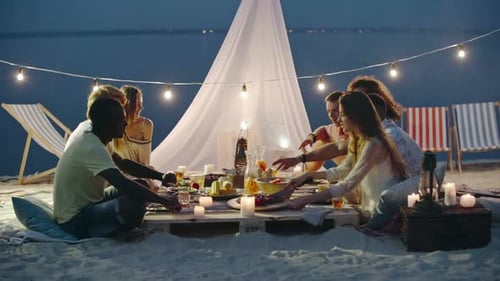 Friends Enjoying Beach Dinner Under String Lights at Night
