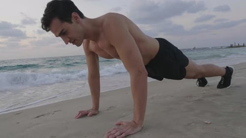 Handsome young male doing push up exercise on beach