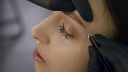Indoor Close-up of a Makeup Master Carefully Plucking Eyebrows with Tweezers