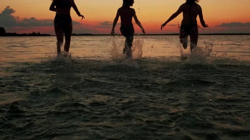 Silhouettes of Children Running at Sunset Into the Water on the Beach