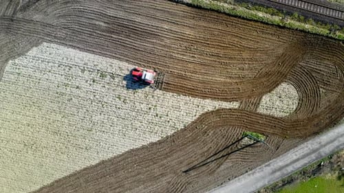 Tractor rojo arando un campo en primavera, vista aérea, Polonia