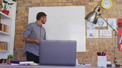 Caucasian male teacher teaching chemistry while looking at laptop in the classroom at school