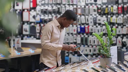Afroamerican Man is Testing Different Models of Smartphones in Digital Equipment Store Choosing