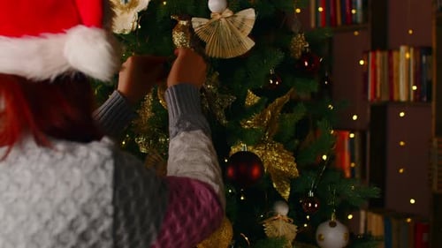 Side View of Woman in Santa Hat Decorating Christmas Tree