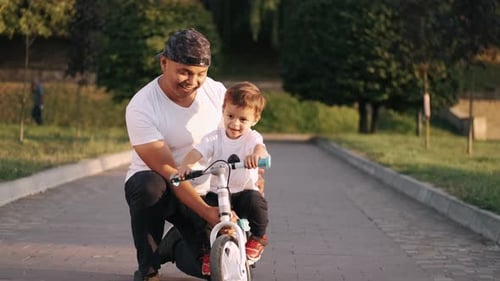 Dad Teaching Son To Drive a Bike in the Summer Park