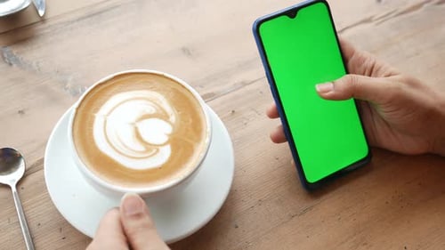 Halten Sie eine Tasse Kaffee und verwenden Sie ein Smartphone mit grünem Bildschirm