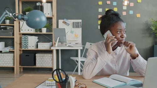 Joyful Mixed Race Girl Speaking on Mobile Phone at Work Sitting at Desk in Office
