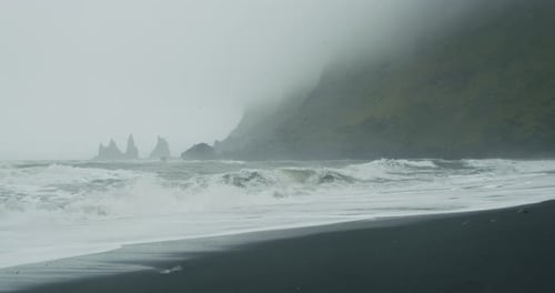 The Black Sand Beach of Reynisfjara with Waves Hitting the Shore on Foggy Rainy Stormy Day
