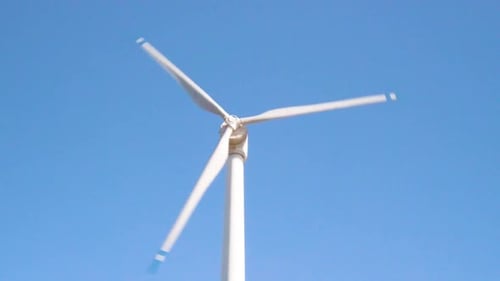 White Wind Turbine Spins Against Clear Blue Sky