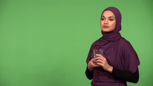 A Young Beautiful Muslim Woman Drinks Water From a Glass Then Smiles at the Camera Green Screen