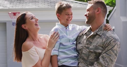 Happy caucasian male soldier embracing his smiling son with wife in garden outside their house