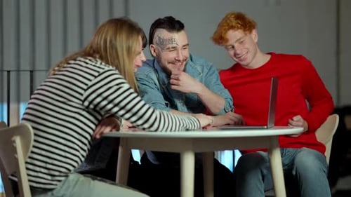 Group of Cheerful Young Millennials Using Laptop Sitting in Cafe