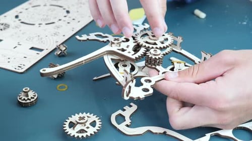 Homme assemblant un jouet mécanique en bois sur une table.