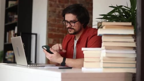 Stylish man sitting at table in home office and using laptop