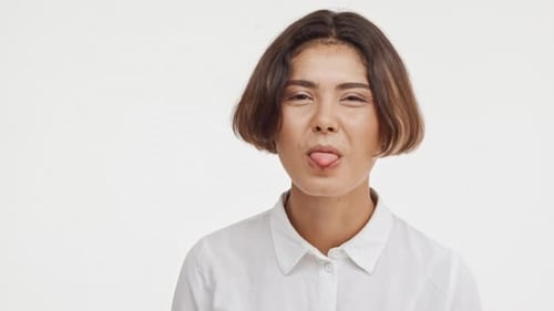 Linda jovem morena do leste asiático em camisa mostrando a língua fazendo caretas sorrindo em branco