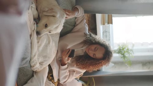 Woman on Sofa With Dog Petting While Using Phone