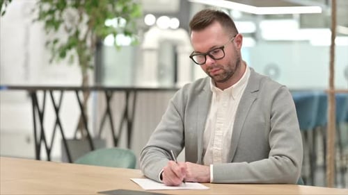 Man in Suit Writing and Contemplating at Desk