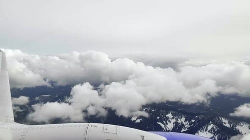 Ego-POV aus einem Flugzeugfenster, während es über die Berge und durch weiße, geschwollene Cl fliegt