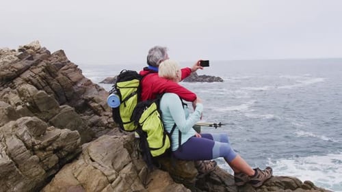 Couple Sits On Rocky Beach and Takes Photos