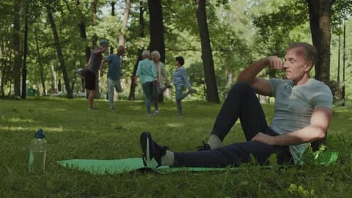 Man Relaxing After Exercise in Park with Group