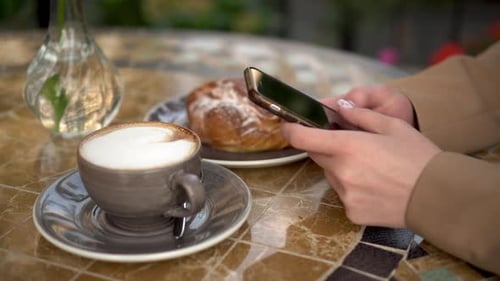 A Young Business Woman Is Sitting in a Cafe and Texting on the Phone Close-up. Girl with Coffee and