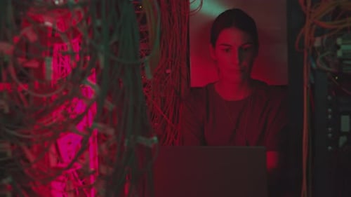 Woman Working in Dark Server Room with Laptop