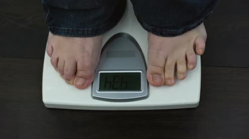 Übergewichtige männliche Füße auf Waagen, Kilogramm nach dem Training messen