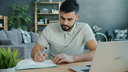 Young Adult Man Writing in Notebook at Home