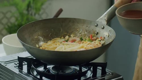 Woman pouring broth into pan with wok noodles