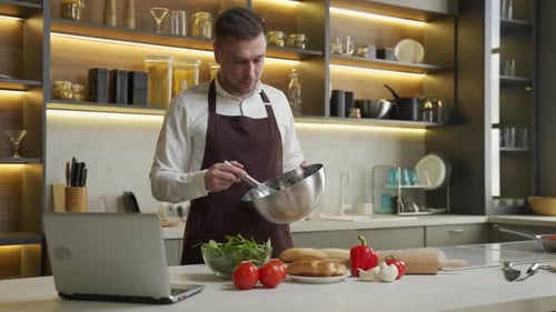 Man Prepares Food While Looking at Laptop