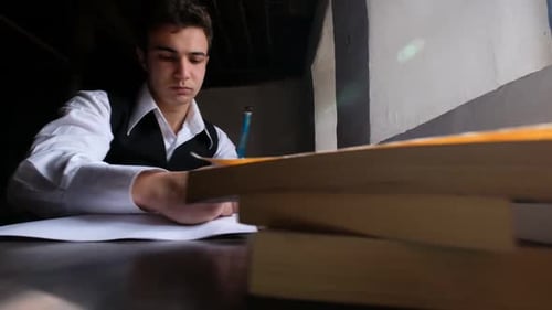 Young Man Writes at Desk Indoors With Books