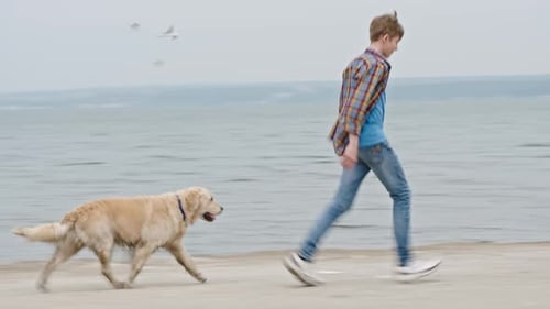 Teenager and Dog Running on Beach Together